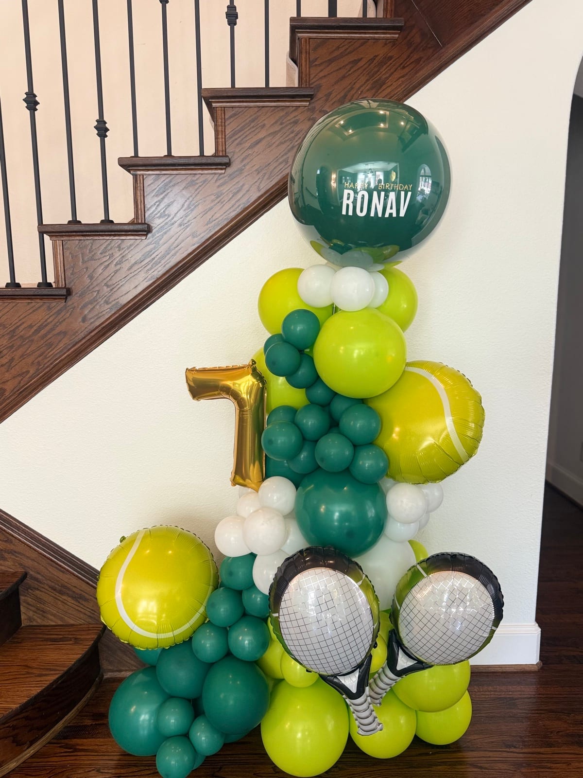 A column of lime and forest balloons hung with foil tennis rackets and a gold number seven