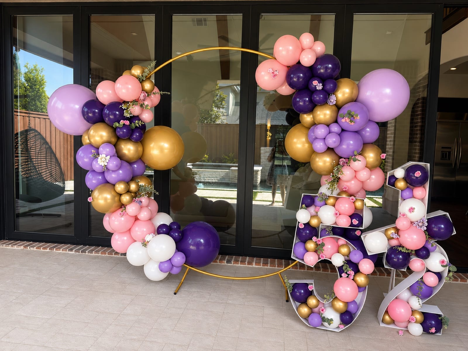 Marquee numerals packed with balloons reading five and a half, beside a gold ring wound in plum, lilac, blush and chrome