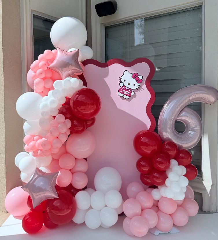 A blush, cherry and white garland wrapping a scalloped pink backdrop, with a pearl number six standing alongside