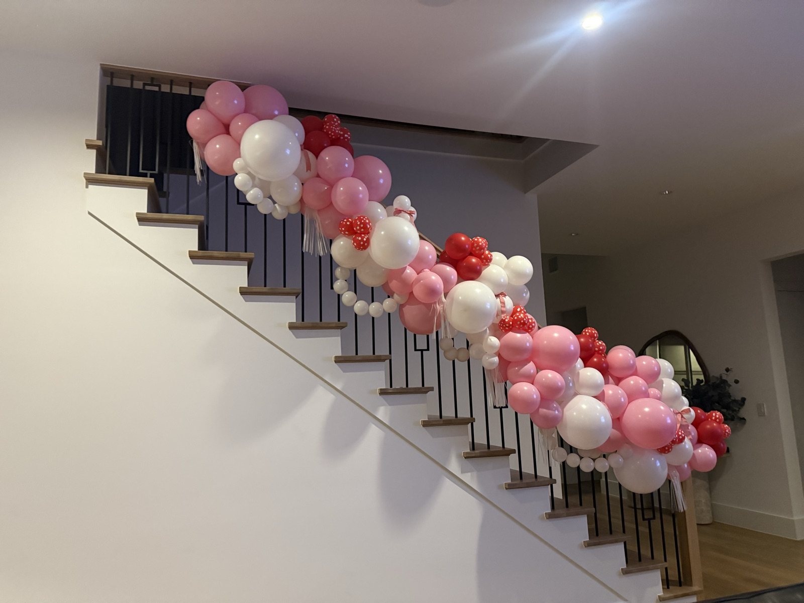 A garland of pink, red and white balloons with polka-dot hearts and tassels running the length of a black iron banister